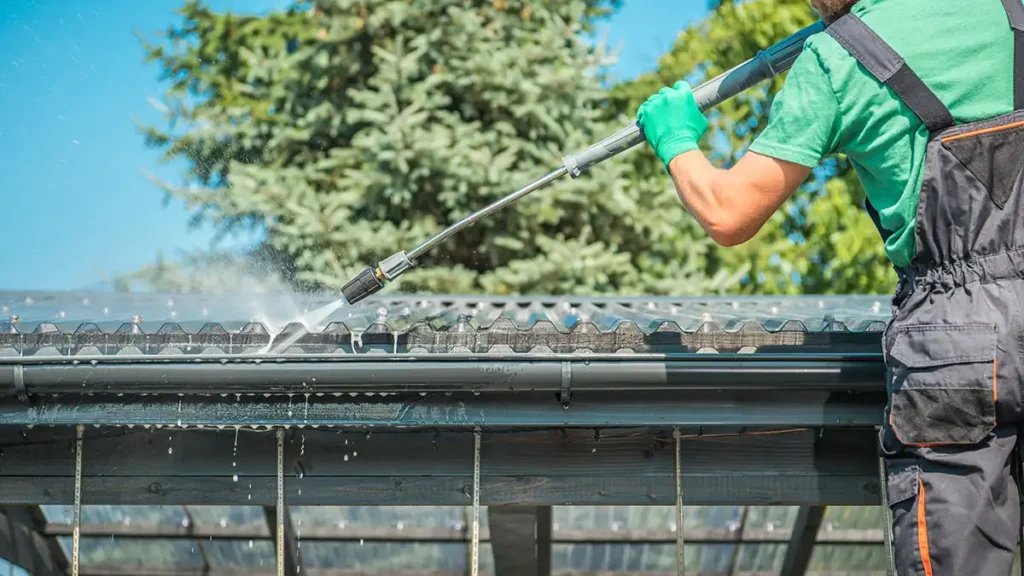 A worker cleaning roof gutters with a pressure washer